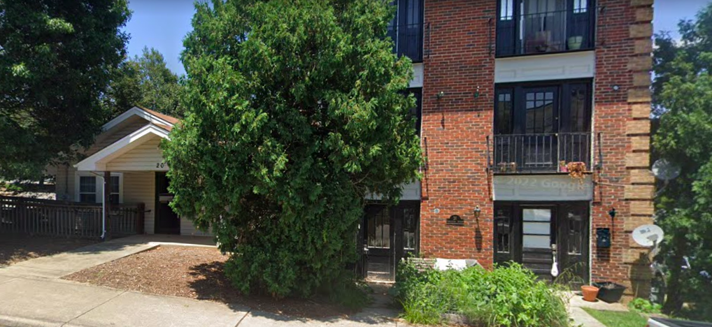 A small single-family home next to a larger apartment building on a tree-lined street.