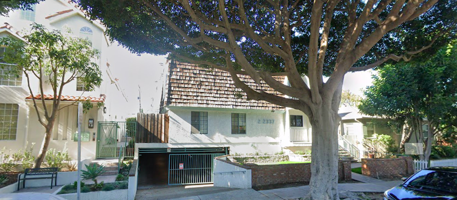 A two story condominium building on a tree-lined street.